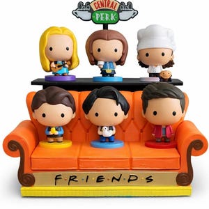 May include: A collectible Friends TV show figurine set. The set includes six chibi-style figures of the main characters, a Central Perk sign, and an orange couch base with the word "FRIENDS". The figures are on a black shelf.