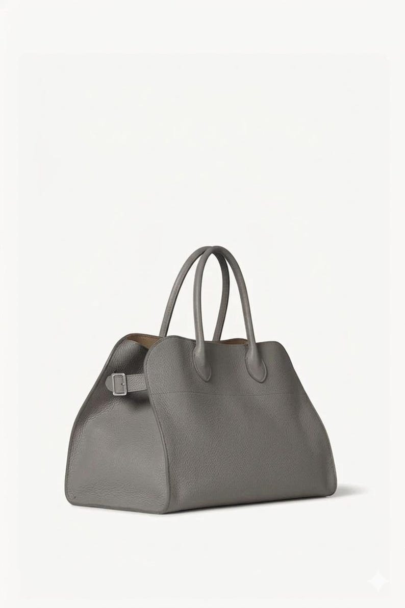 Peut inclure: Un sac fourre-tout en cuir gris avec deux poign&eacute;es sup&eacute;rieures et une forme rectangulaire. Le sac est dot&eacute; d'une fermeture &agrave; boucle sur le c&ocirc;t&eacute; et d'une surface textur&eacute;e. L'int&eacute;rieur est de couleur marron clair.