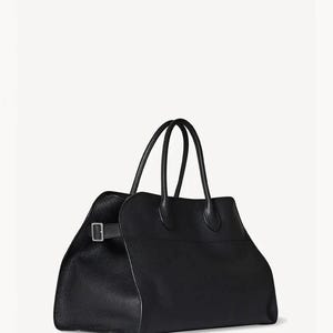 Peut inclure: Un sac fourre-tout en cuir noir avec deux poign&eacute;es sup&eacute;rieures et une forme rectangulaire. Le sac a une fermeture &agrave; boucle et une surface textur&eacute;e. Le sac est pos&eacute; sur un fond blanc.