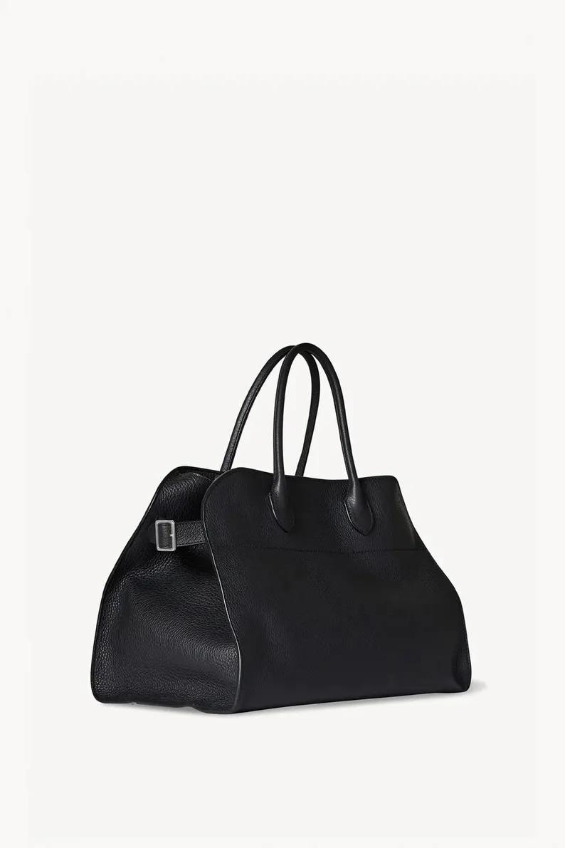 Peut inclure: Un sac fourre-tout en cuir noir avec deux poign&eacute;es sup&eacute;rieures et une forme rectangulaire. Le sac a une fermeture &agrave; boucle et une surface textur&eacute;e. Le sac est pos&eacute; sur un fond blanc.