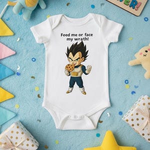 May include: White baby bodysuit featuring a cartoon character with a cookie, and the text "Feed me or face my wrath!". The image is surrounded by toys and gifts on a blue surface.