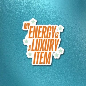 May include: A white sticker with the text "MY ENERGY IS A LUXURY ITEM" in orange, outlined in white. The sticker has a white border and is decorated with small green star shapes. The background is a textured teal color.