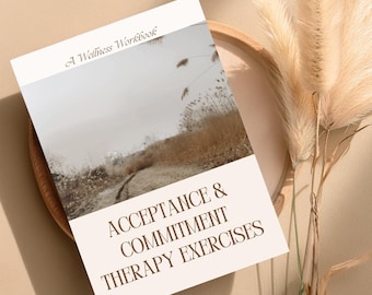 Puede incluir: Un cuaderno de trabajo de bienestar titulado "Acceptance & Commitment Therapy Exercises" con una imagen de paisaje en la portada. El libro está colocado sobre una bandeja de madera con hierba ornamental seca en el fondo. La paleta de colores es neutra, con tonos beige y marrón.