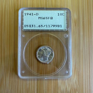 May include: A silver coin from 1941-D, encapsulated in a clear plastic holder. The holder has a green label with text including "10C" and "MS65FB". The coin features a profile image and is centered within the holder.