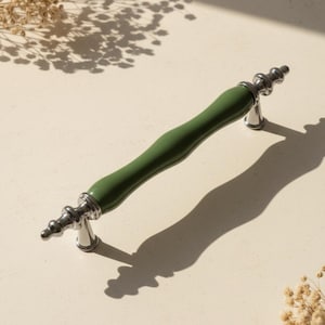 May include: A green and silver cabinet pull handle. The handle has a curved, olive green centre section and silver-coloured, decorative end pieces. The handle is approximately 15 cm long.