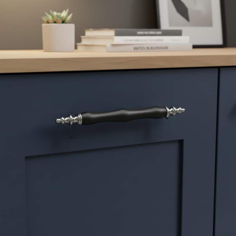 May include: A close-up of a navy blue cabinet door featuring a black and silver handle. The handle has a cylindrical, dark shape with decorative silver detailing at each end. The handle is a stylish addition.