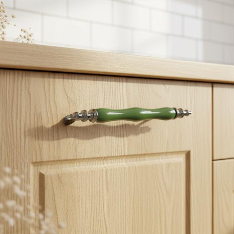 May include: A wooden cabinet door featuring a green and silver handle. The handle is a curved, cylindrical shape with a glossy green centre and silver accents. The cabinet door has a recessed panel design.