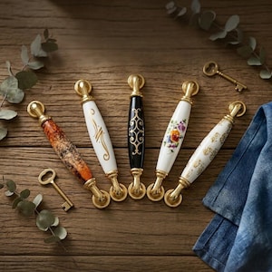 Könnte beinhalten: Eine Sammlung dekorativer Schrankgriffe mit Messingbeschlägen. Die Griffe weisen verschiedene Designs auf, darunter Blumenmuster, abstrakte Designs und ein schwarz-goldenes Muster. Zwei antike Schlüssel sind ebenfalls vorhanden.
