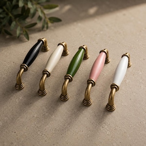 May include: Five cabinet pulls with brass fittings and ceramic handles in black, cream, green, pink, and white. The pulls are arranged in a row on a neutral surface.