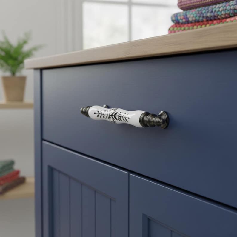 May include: A navy blue cabinet with a light wood top and a white and black floral patterned handle. The cabinet has a paneled door design. The handle is a decorative element. The cabinet is set against a neutral background.