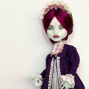 May include: A custom doll with pale green skin, deep purple hair, and a matching purple dress. The dress features white lace trim and cuffs, with a white underskirt. The doll wears a white and pink lace headpiece.