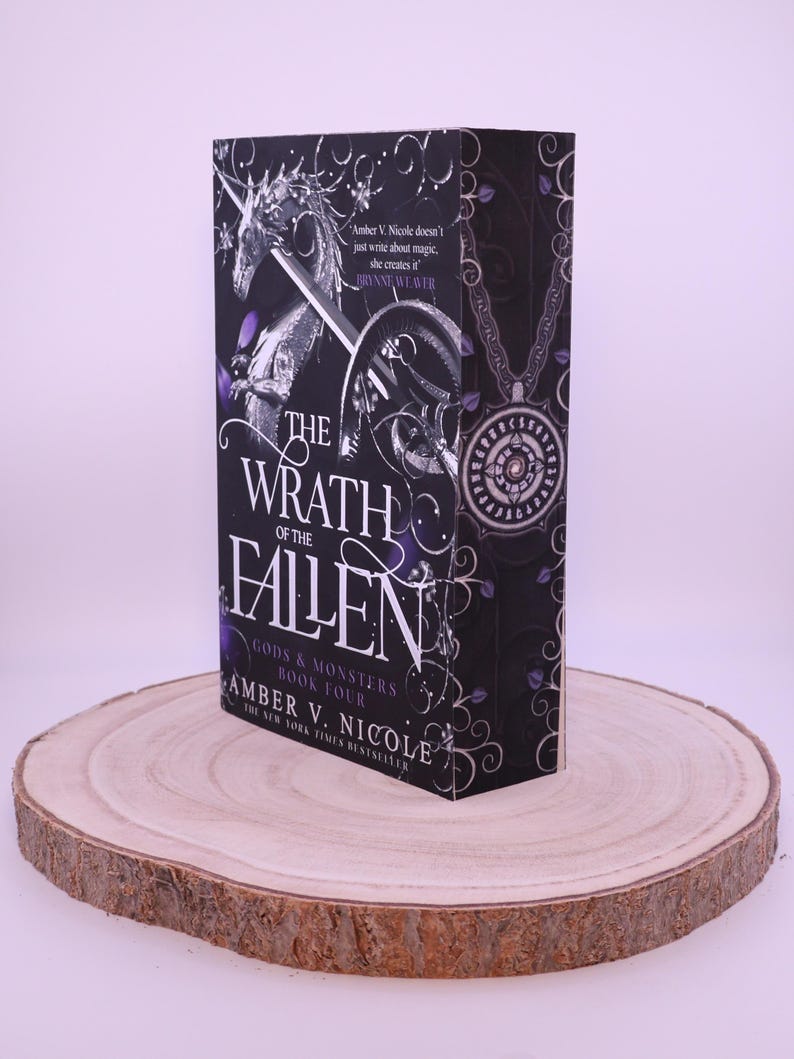 Peut inclure: Un livre &agrave; couverture rigide intitul&eacute; "The Wrath of the Fallen" par Amber V. Nicole. Le livre pr&eacute;sente une couverture noire avec des accents argent&eacute;s et violets, et un dessin d'une licorne et d'une &eacute;p&eacute;e. Le livre est pr&eacute;sent&eacute; sur une tranche de bois ronde.