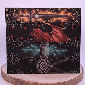 Peut inclure: Bo&icirc;te sur le th&egrave;me de la fantaisie avec des illustrations d'une &eacute;p&eacute;e et d'&eacute;clairs, d'un dragon rouge et d'un marteau avec des &eacute;clairs. La bo&icirc;te a un fond noir avec des &eacute;l&eacute;ments floraux et est pr&eacute;sent&eacute;e sur une tranche de bois.