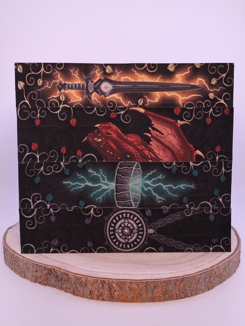 Peut inclure: Bo&icirc;te sur le th&egrave;me de la fantaisie avec des illustrations d'une &eacute;p&eacute;e et d'&eacute;clairs, d'un dragon rouge et d'un marteau avec des &eacute;clairs. La bo&icirc;te a un fond noir avec des &eacute;l&eacute;ments floraux et est pr&eacute;sent&eacute;e sur une tranche de bois.