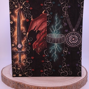 Peut inclure: &OElig;uvre d'art sur le th&egrave;me de la fantaisie avec une &eacute;p&eacute;e, un dragon rouge, un anneau avec des &eacute;clairs et un pendentif. L'&oelig;uvre est sur un fond sombre avec des volutes d&eacute;coratives et est pr&eacute;sent&eacute;e sur une tranche de bois.