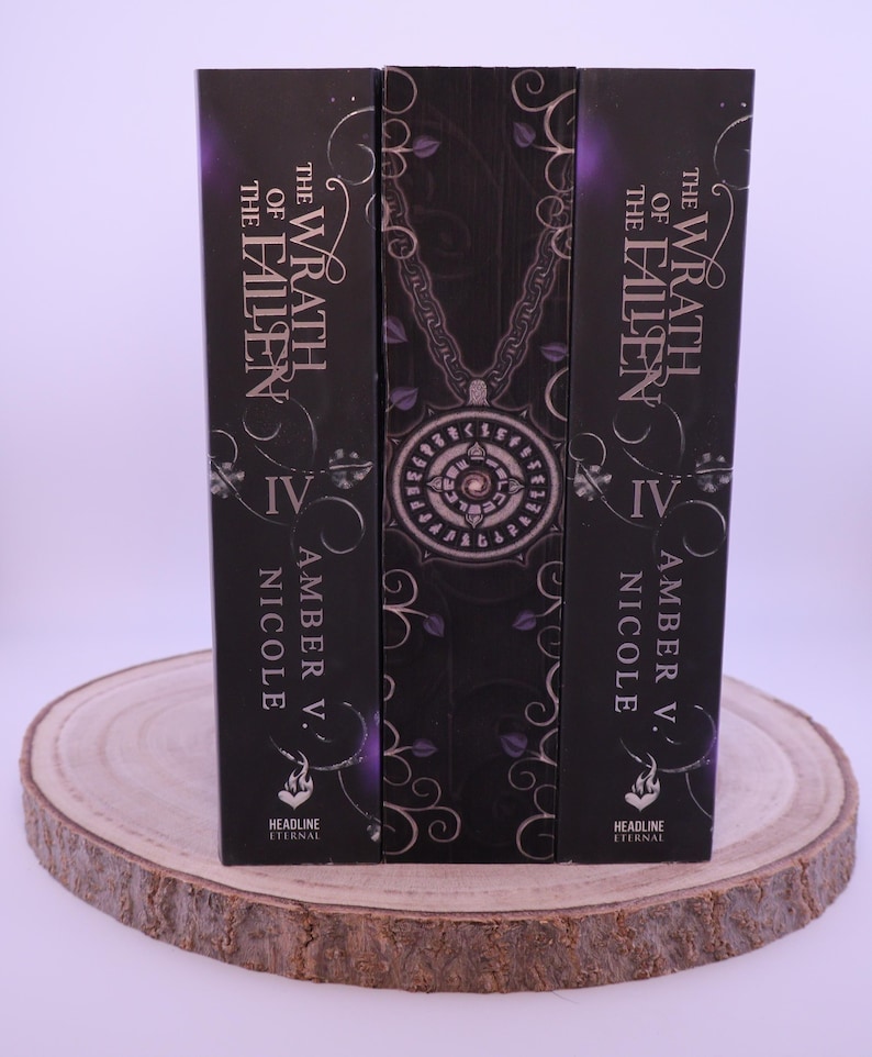Peut inclure: Trois livres &agrave; couverture rigide avec des couvertures sombres, avec le titre "The Wrath of the Fallen" et le nom de l'auteur, Amber V. Nicole. Les dos sont noirs avec des accents violets et des motifs d&eacute;coratifs. Les livres sont pr&eacute;sent&eacute;s sur une tranche de bois.