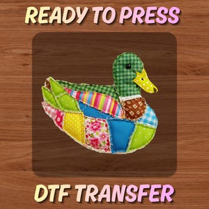 May include: A colorful, patchwork duck design with a green checkered head and yellow beak. The body features various fabric patterns, including floral, polka dot, and striped designs. The text "READY TO PRESS" and "DTF TRANSFER" are displayed above and below the duck.