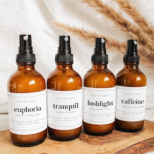 Peut inclure: Quatre flacons pulvérisateurs en verre ambré avec des vaporisateurs noirs et des étiquettes blanches. Les étiquettes indiquent "euphoria", "tranquil", "lushlight" et "caffeine". Les flacons sont sur une planche de bois avec des plantes séchées en arrière-plan.