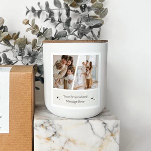 Peut inclure: Une bougie blanche avec un couvercle en bois et une étiquette rectangulaire avec deux photos de famille. L'étiquette comprend le texte "Your Personalized Message Here" et des étoiles décoratives. La bougie est posée sur une surface à motifs marbrés.