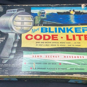 Puede incluir: Juego vintage Navy Blinker Code Lite en caja original. La caja presenta un gráfico de un marinero usando la luz y el texto "Enviar y recibir código Morse oficial". Incluye 2 luces de código.