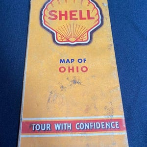 May include: Vintage Shell Map of Ohio. The map features the Shell logo, a red and yellow seashell, and the text "Map of Ohio" and "Tour with Confidence". The map has a yellow background with some wear and tear.