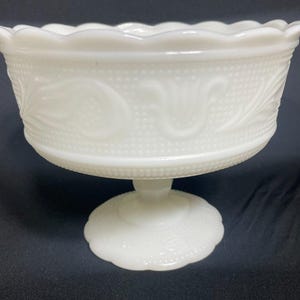 Puede incluir: Un cuenco blanco con pedestal de estilo vintage. El cuenco presenta un borde festoneado y un patrón detallado de puntos y diseños florales. Se apoya en una base de pedestal corta.
