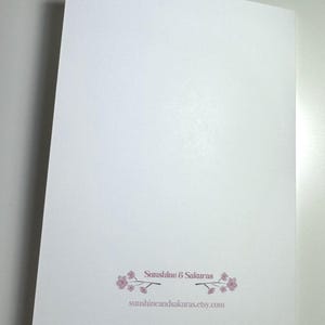 K&ouml;nnte beinhalten: Eine wei&szlig;e Karte mit dem Text "Sunshine & Sakuras" und der Website-Adresse. Der Text ist hellrosa, mit einem floralen Design. Die Karte ist abgewinkelt und zeigt die R&uuml;ckseite.