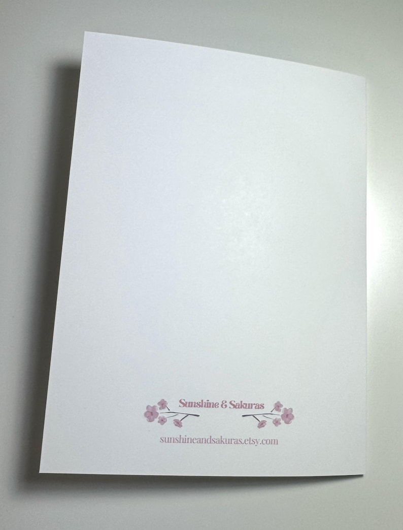 K&ouml;nnte beinhalten: Eine wei&szlig;e Karte mit dem Text "Sunshine & Sakuras" und der Website-Adresse. Der Text ist hellrosa, mit einem floralen Design. Die Karte ist abgewinkelt und zeigt die R&uuml;ckseite.