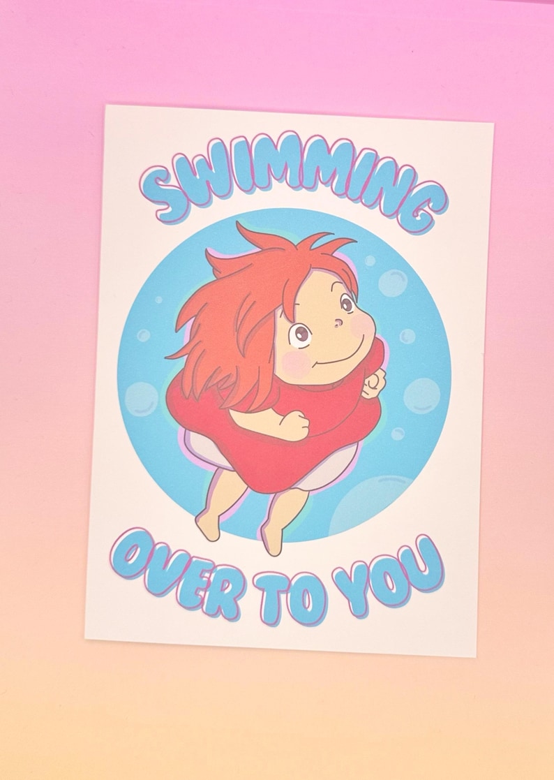 K&ouml;nnte beinhalten: Ein Druck mit einer Zeichentrickfigur mit roten Haaren und einem roten Kleid, die in einem blauen Kreis mit Blasen schwebt. Der Text "SWIMMING OVER TO YOU" steht in Blau &uuml;ber und unter der Figur.