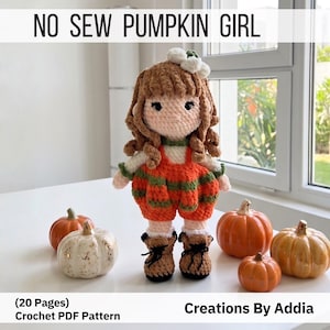 May include: A crochet doll with brown hair, a white flower accessory, and an orange and green striped outfit, standing among four small decorative pumpkins. The text reads NO SEW PUMPKIN GIRL, 20 Pages, Crochet PDF Pattern, and Creations By Addia.