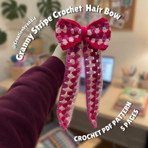 Pode incluir: Um laço de cabelo de crochê feito à mão em um padrão de listras de vovó. O laço apresenta tons de rosa e branco, com caudas longas e penduradas. O texto na imagem diz "Granny Stripe Crochet Hair Bow" e "CROCHET PDF PATTERN 5 PAGES."
