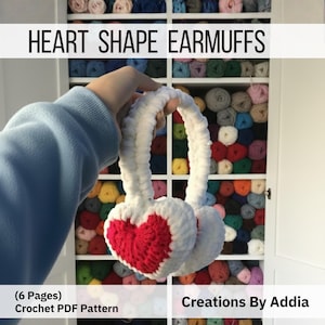 Puede incluir: Orejeras blancas y rojas en forma de corazón. Las orejeras son blancas con un diseño de corazón rojo. El texto "HEART SHAPE EARMUFFS" está en la parte superior de la imagen. El texto "(6 Pages) Crochet PDF Pattern" y "Creations By Addia" están en la parte inferior.