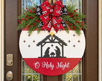 May include: A round wooden door sign featuring a black nativity silhouette on a white background with a red bottom section. The text O Holy Night is written in white script. It is topped with a large red and black plaid bow and greenery.