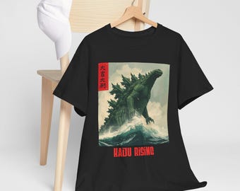 May include: Black t-shirt featuring a green Godzilla graphic rising from the ocean, with the text "KAIJU RISING" in red. The shirt also has Japanese text in a red box. A white hat hangs on a wooden chair.