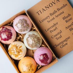May include: A box of TIANOVA luxury bath bombs in various colors, including pink, orange, and green, with dried flower and herb toppings. The box is open, revealing six bath bombs with different scent aromas, such as Lavender and Rose.