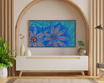 May include: A rectangular wall art piece featuring two large, stylized blue and purple flowers with orange centers against a textured teal and green background, displayed in a black frame above a white media console with light wood accents.