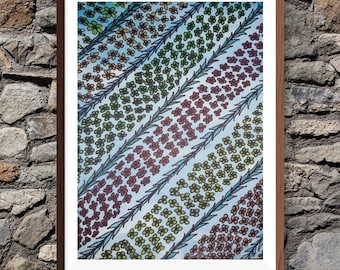 May include: A framed wall art print featuring a repeating pattern of diagonal bands filled with small, colorful hand-drawn flowers in shades of red, yellow, and green, separated by thin, textured, light blue leaf-patterned dividers.