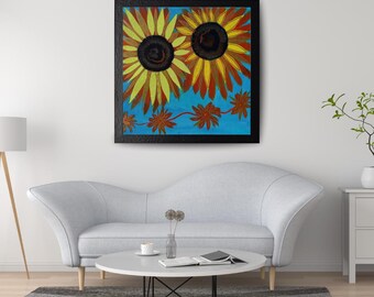 May include: A square framed wall art piece featuring two large sunflowers with yellow and orange petals and dark brown centers set against a bright blue background, with a horizontal vine of smaller reddish-brown flowers across the bottom.