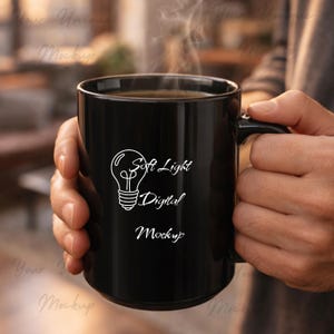 May include: A black coffee mug with the text "Soft Light Digital Mockup" and a lightbulb graphic in white. The mug is filled with a dark liquid, and steam rises from the top. The mug is held by a person.