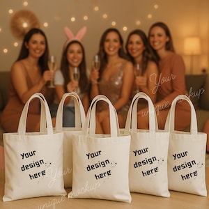 May include: Five off-white canvas tote bags with the text "Your design here" in black. The bags have a simple design with handles. The background features a group of people holding champagne flutes.