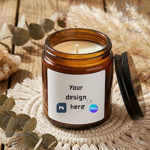 May include: A brown glass jar candle with a white label that reads "Your design here." The candle has a black lid and a white wick. The candle sits on a woven coaster with dried plants in the background.