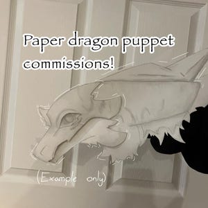Peut inclure: Une marionnette dragon en papier blanc avec des ombres grises et des traits faciaux définis. Le texte sur l'image indique : Paper dragon puppet commissions! (Example only). La marionnette a un museau pointu, de grands yeux et des bords dentelés.