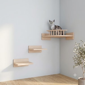 Può includere: Un set di mobili da parete per gatti in legno chiaro composto da due gradini rettangolari singoli e una piattaforma angolare più grande con una ringhiera semicircolare. Un gatto grigio tigrato è seduto sulla piattaforma superiore.