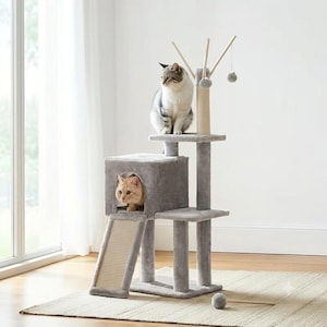 May include: A multi-level cat tree covered in soft gray plush fabric, featuring a square enclosed cubby, a sisal-wrapped scratching ramp, and a top platform. A gray and white cat sits on top, while an orange cat peeks from the cubby entrance.