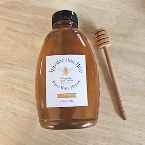 May include: A bottle of Appalachian Hive Pure Raw Sourwood Honey, 24 oz (1.5 lbs), with a wooden honey dipper. The label features a bee illustration and text. The honey is amber-colored.