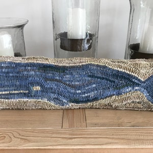 May include: A blue whale pillow with a beige background. The pillow is made of woven fabric and has a textured surface.