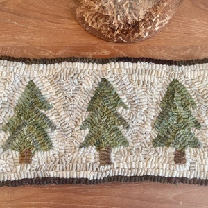 May include: A white and brown rug with a design of three green trees. The rug has a brown border.
