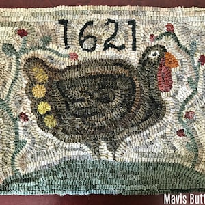 Peut inclure: Un tapis en laine crocheté brun et blanc avec un motif de dinde et le nombre 1621. La dinde est entourée de vignes vertes avec des fleurs rouges. Le tapis a une bordure verte.