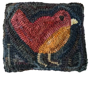 May include: Handmade, square rug featuring a bird design. The bird has a red body, yellow chest, and is set against a dark blue background. The rug is made of textured, looped fabric, giving it a rustic, handcrafted appearance.