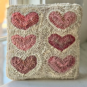 May include: A white throw pillow with a pink heart pattern. The pillow is made of a soft, textured fabric and has a subtle vintage look.